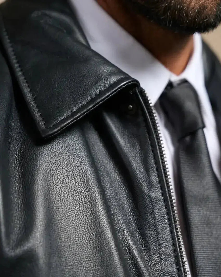 Close-up of a black leather jacket with a zipper, worn by a person.