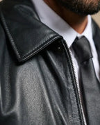 Close-up of a black leather jacket with a zipper, worn by a person.