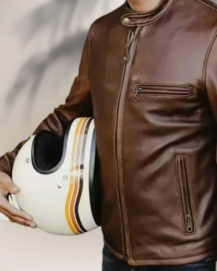 Person wearing a brown leather jacket holding a white helmet with black and orange stripes.